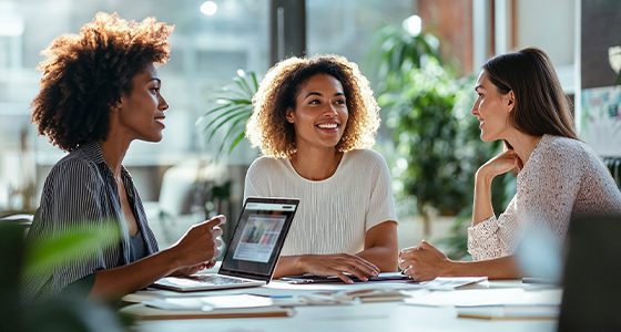 Three women talking around a table in a bright office