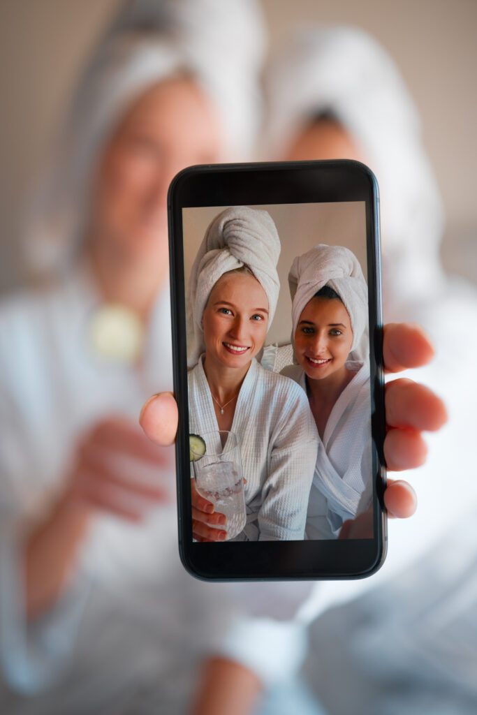 Two friends in towel head wraps taking a photo on a phone