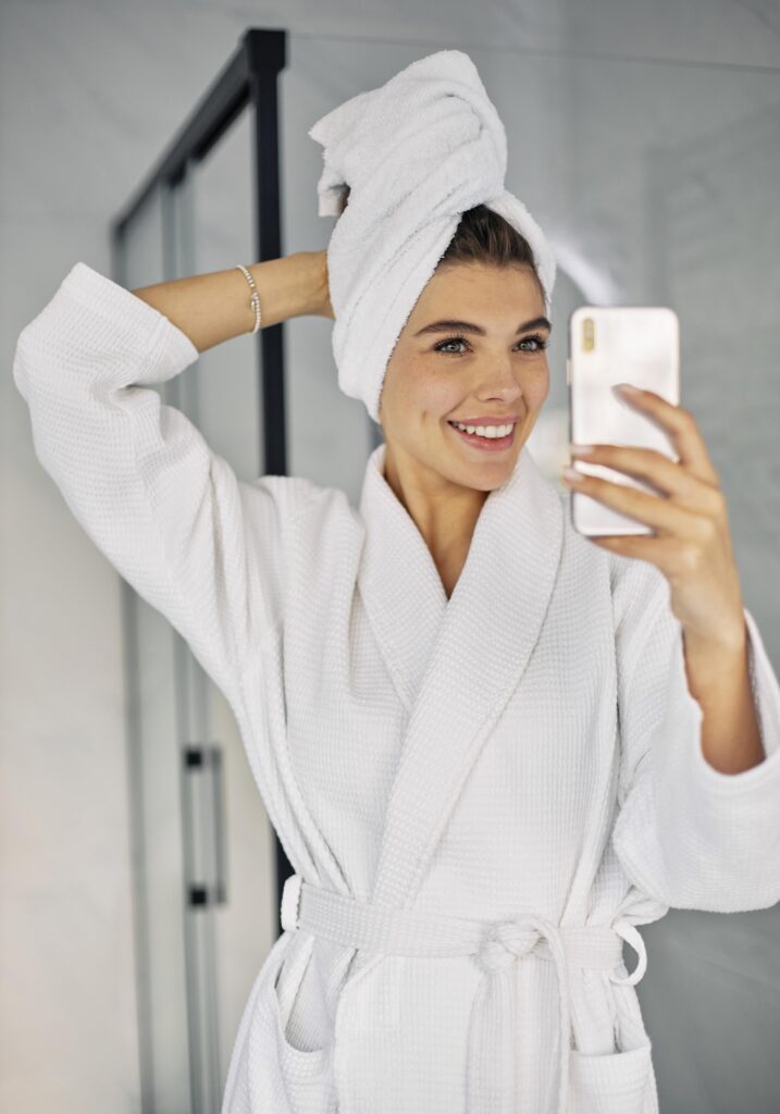 Woman in a white robe and towel wrap taking a mirror selfie
